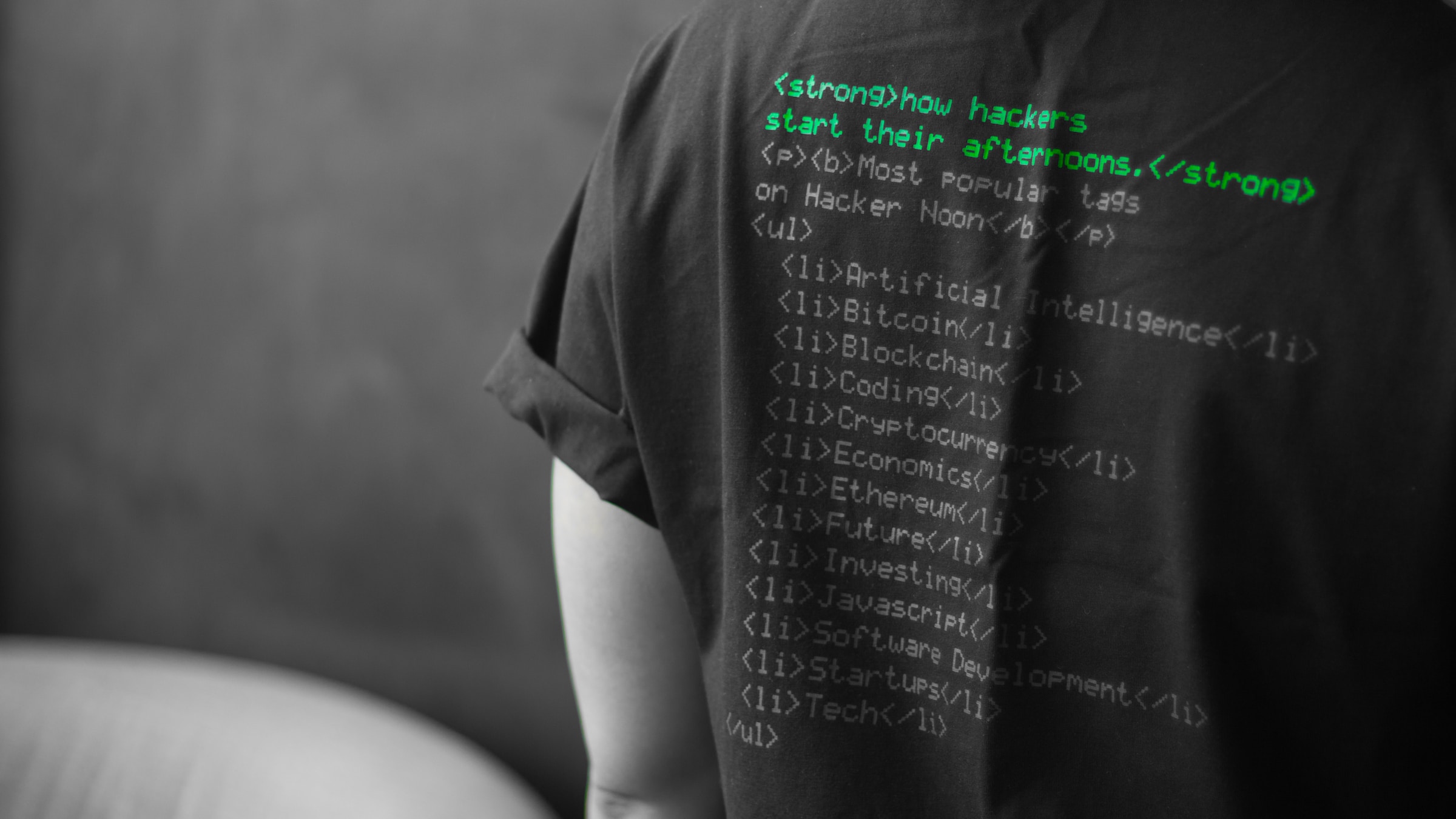 Person standing with back facing camera, wearing a t-shirt featuring hacking-related HTML code in matrix green signifying the importance of web security.